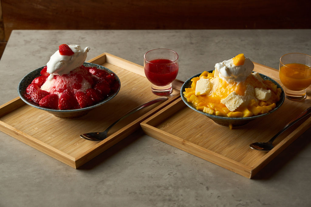 Strawberry and mango cheesecake kakigori side by side on bamboo trays